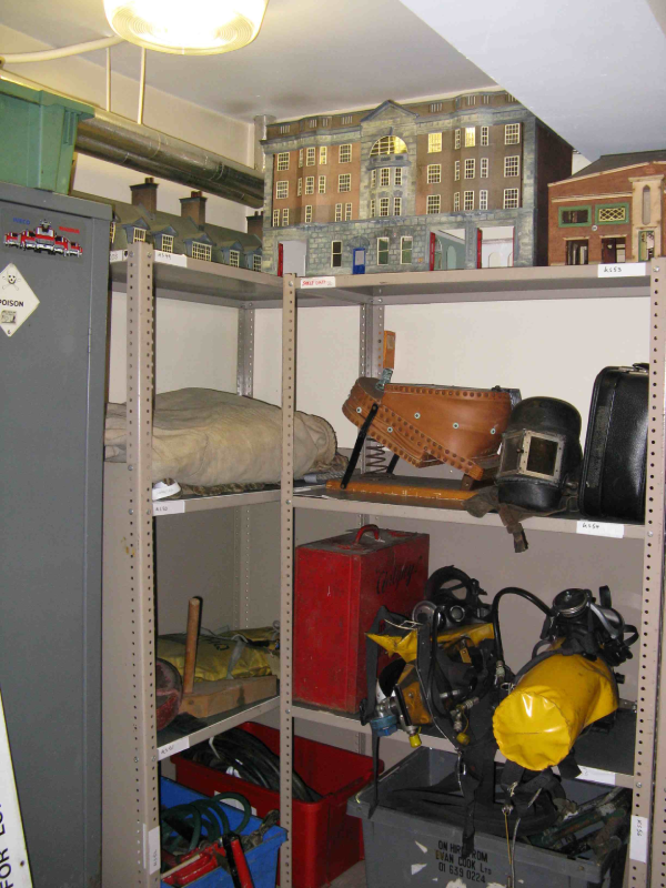 Shelving in a basement with fire brigade items including breathing equipment, models houses and bellows